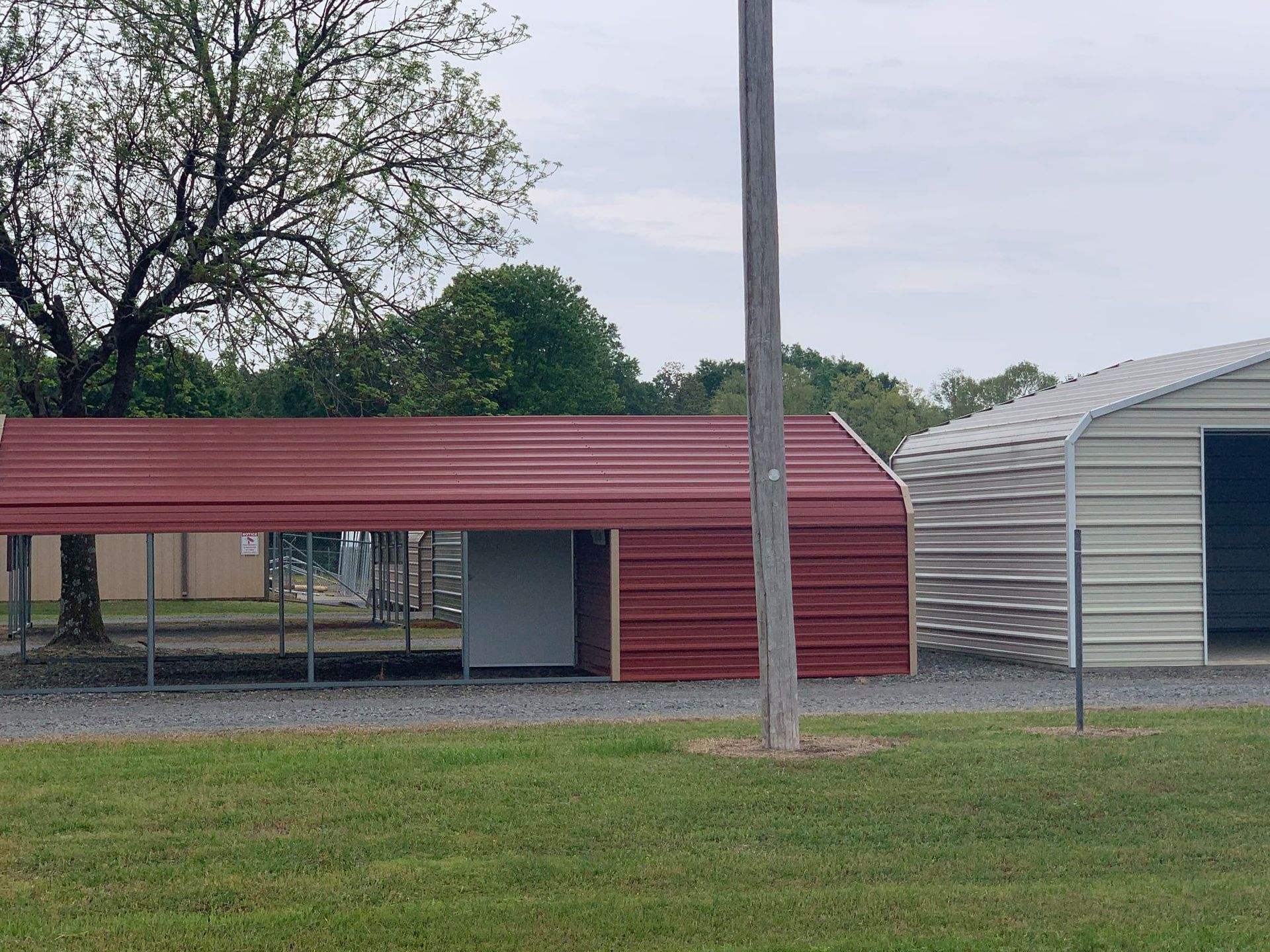 Red and tan metal buildings with a grass field and trees.