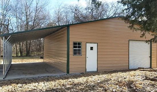 Tan metal building with attached carport, green trim, white doors, and window, outdoors.