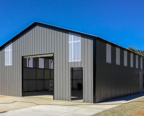 Gray metal building with black trim and large open garage door against a blue sky.