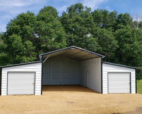 White metal shed with two garage doors and open center, gravel ground, trees in background.