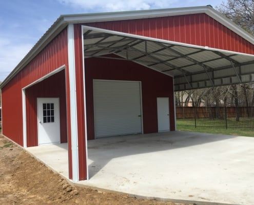 Red metal building with a carport, white doors, and concrete floor.