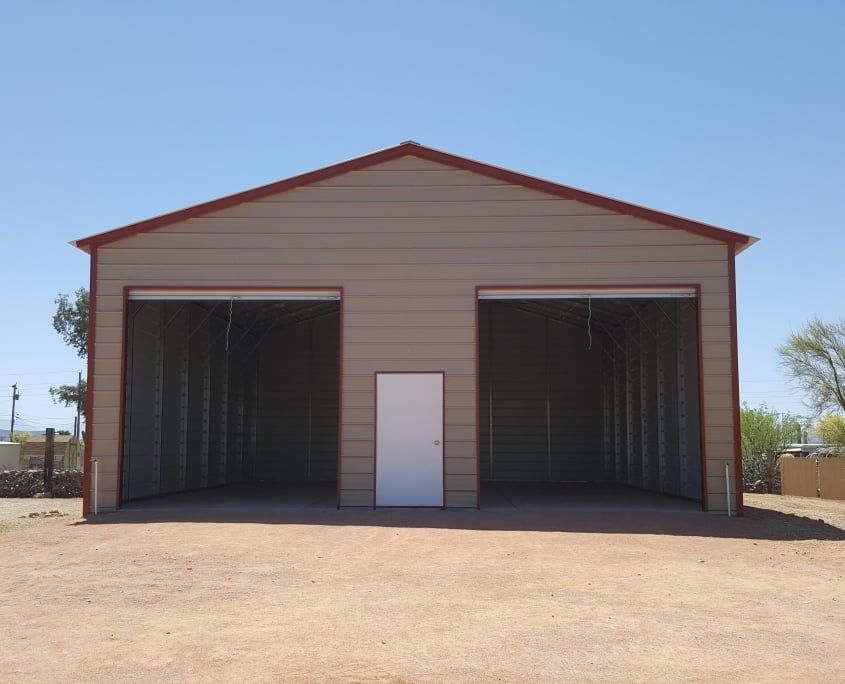Tan metal garage with red trim, two open bays, and a white door.