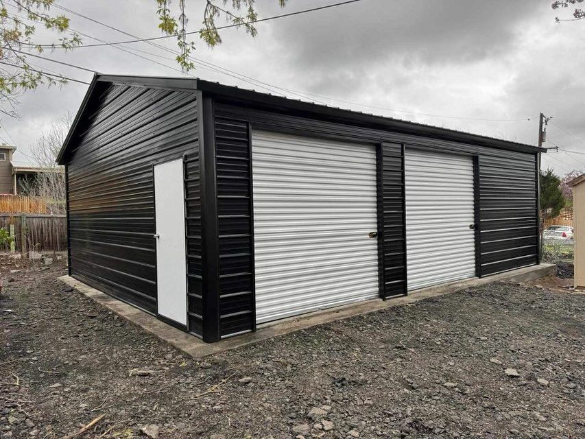 Black metal garage with three doors and a white entry door, in a gravel yard.
