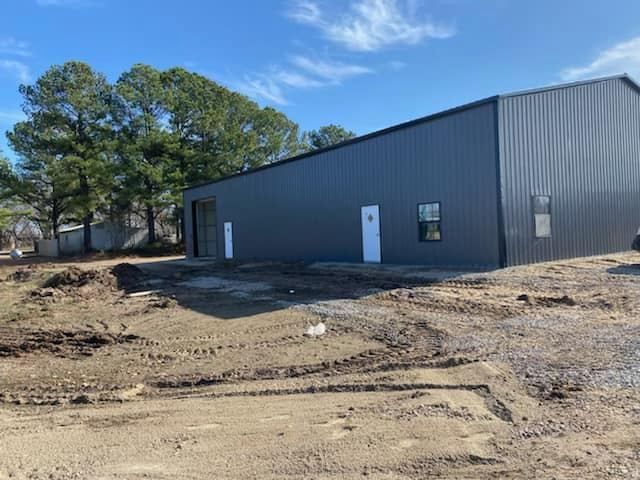 A gray metal building with two white doors, a window, and dirt foreground.