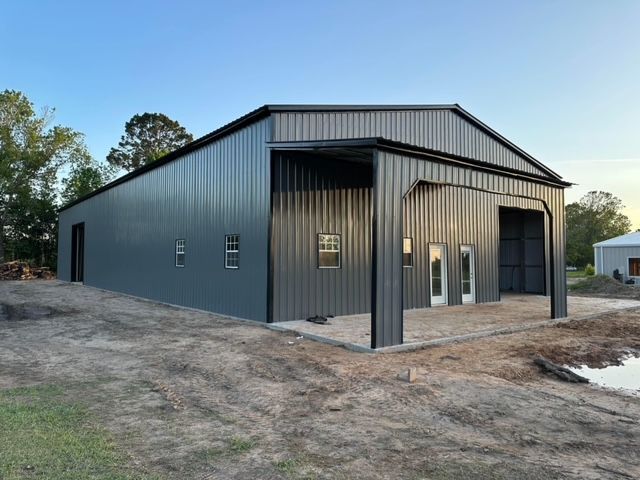 Gray metal building with large open bays, windows, and a sloped roof, outdoors.