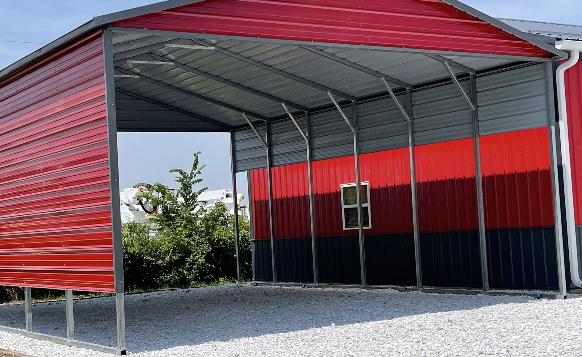 Red and gray metal carport with open front, gravel base, and red, black, and gray siding.