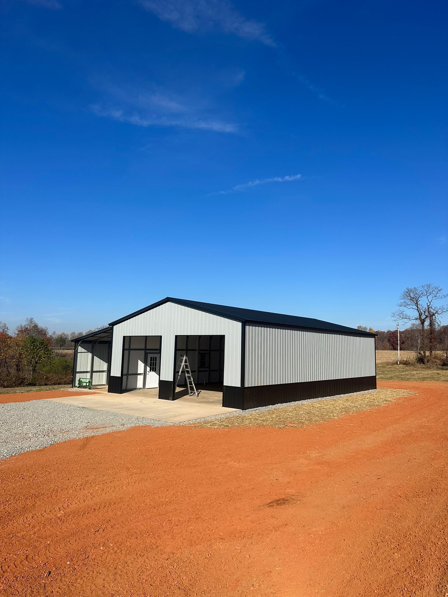 Metal building with black trim, white walls, and open garage doors under a blue sky.