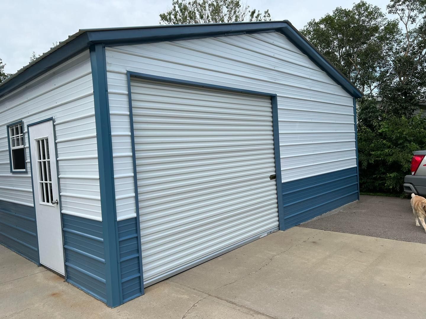 Blue and white metal garage with roll-up door, side door, and concrete driveway.
