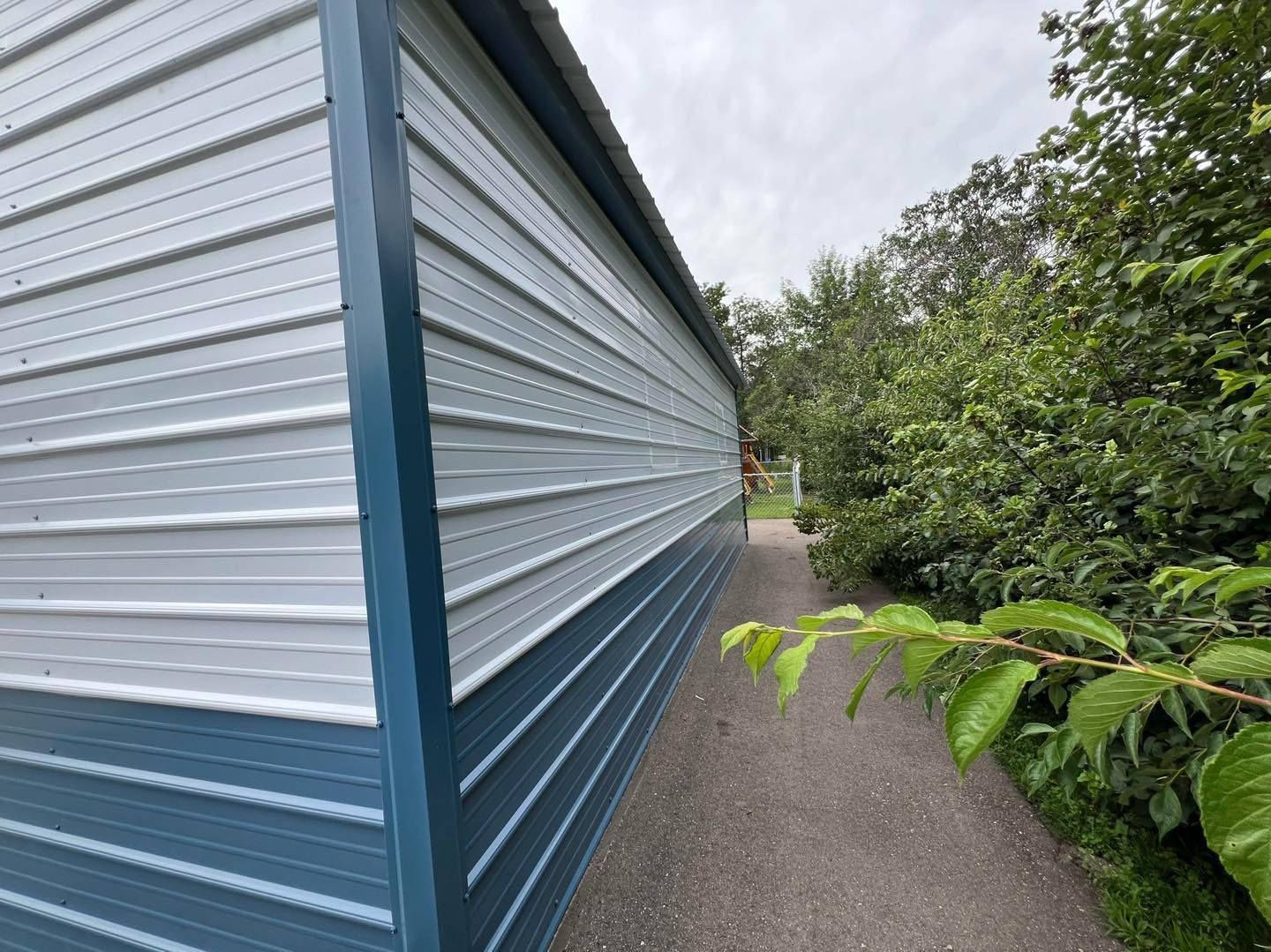 Blue and white metal building with a narrow path and greenery alongside.