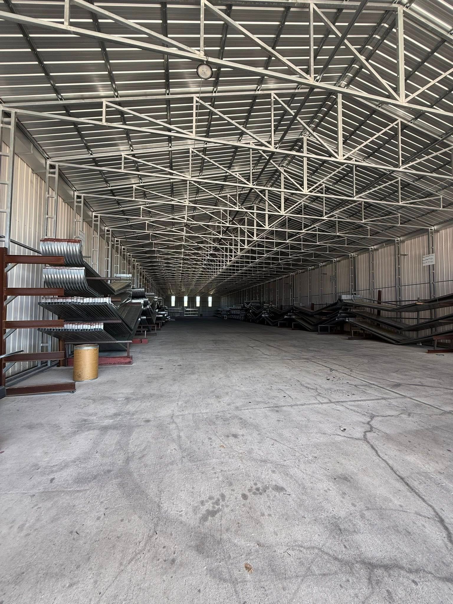 Interior of a large warehouse with metal roofing, storing sheet metal and other materials.