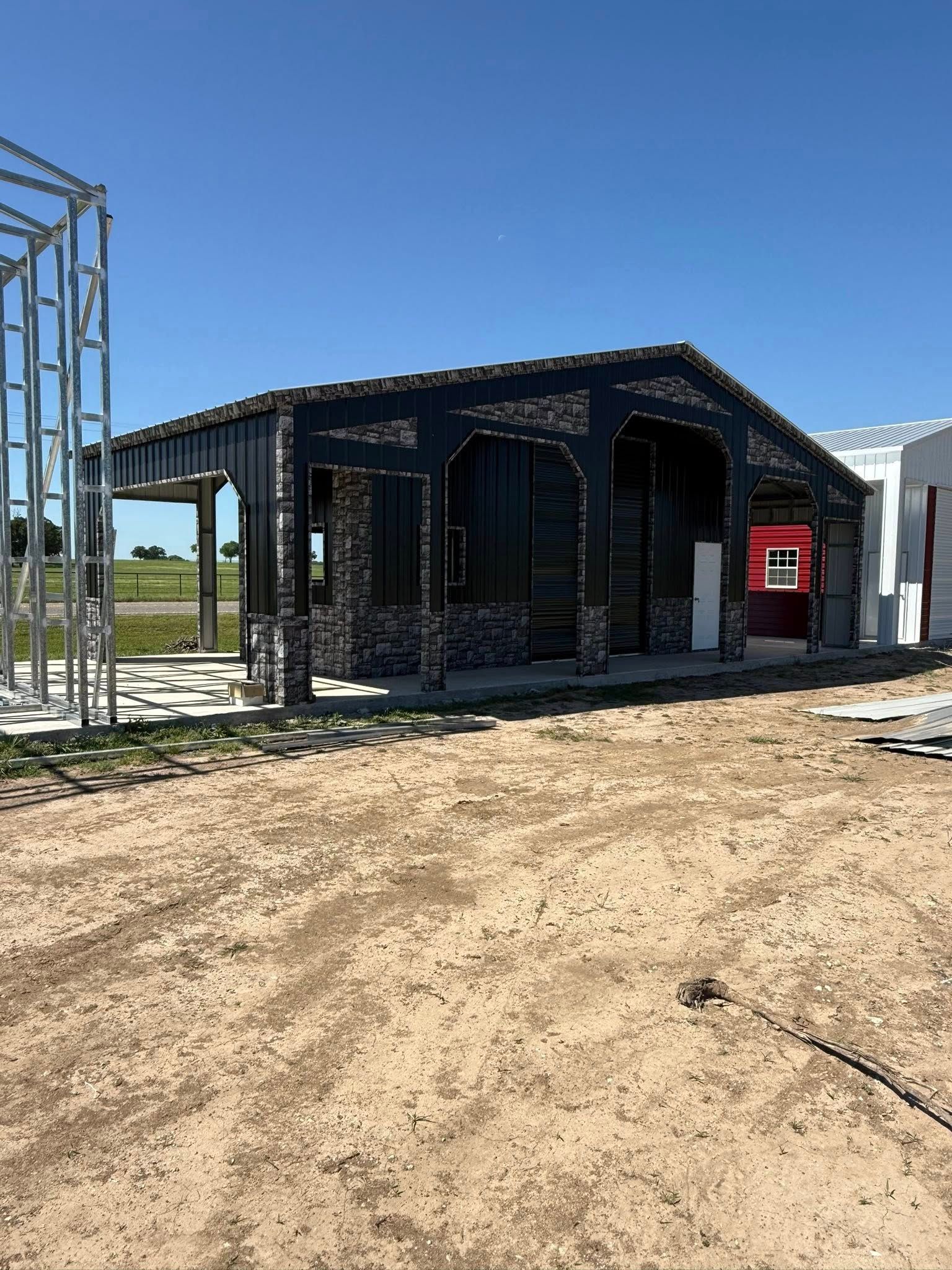 Building under construction with black facade and brick detail against a blue sky.
