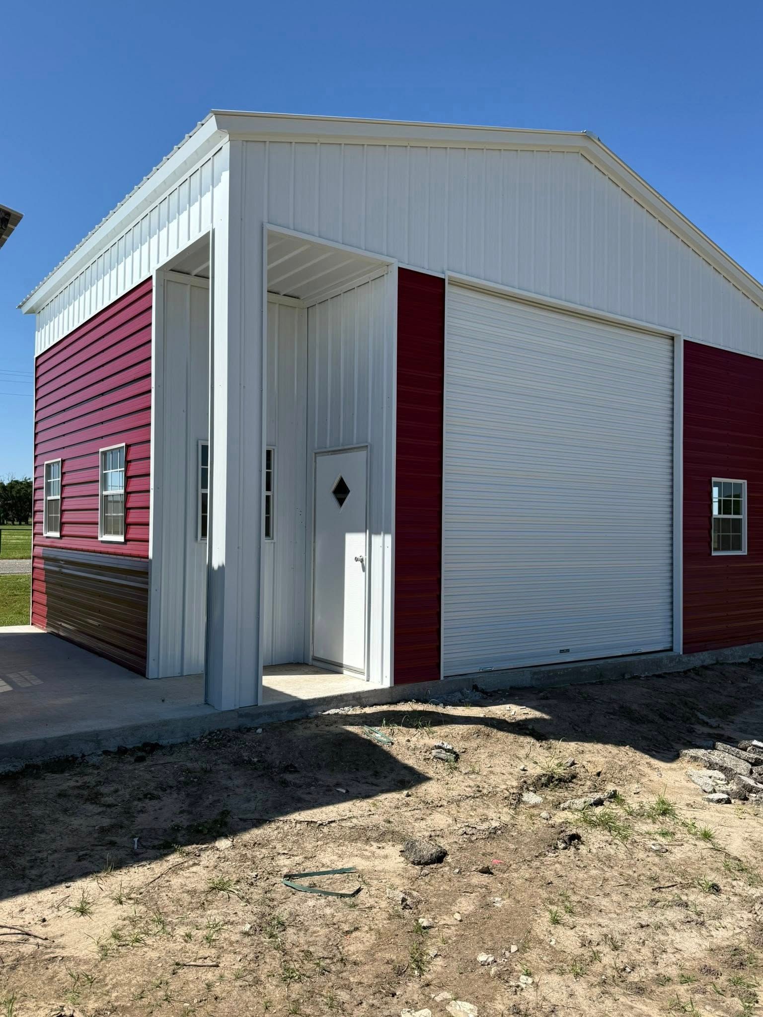 Red and white metal building with large garage door, small door, and windows, outdoors.