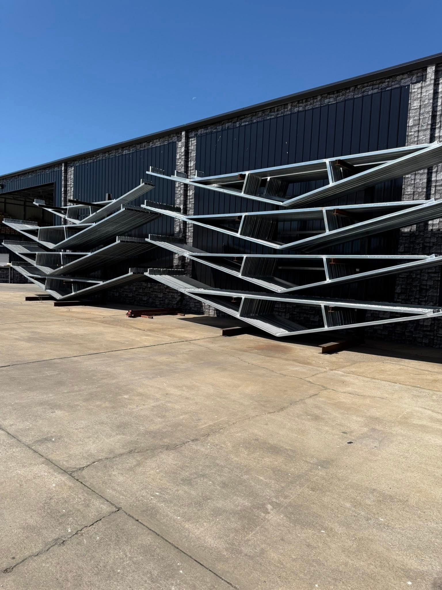 Metal scaffolding stacked outdoors in front of a dark building under a clear blue sky.