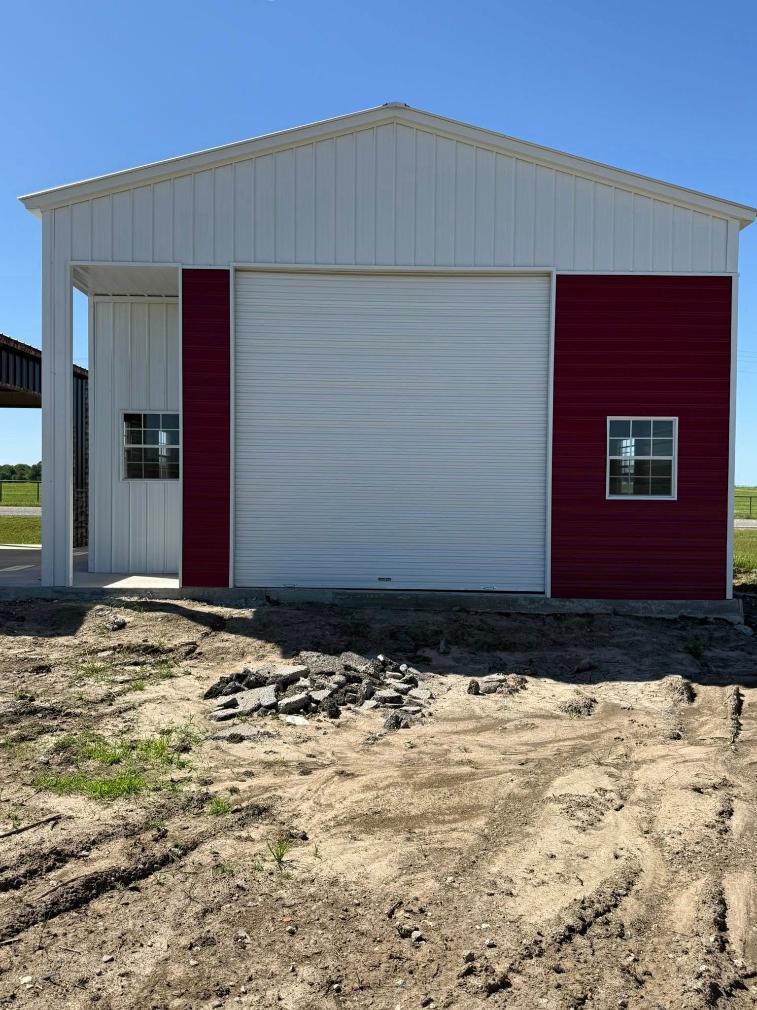 Red and white metal building with a closed garage door, two windows, and a dirt foreground.