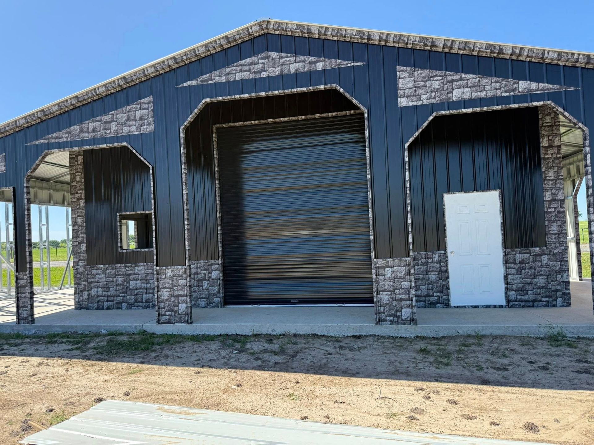 Black metal building with stone accents, large garage door, small window, and white door.