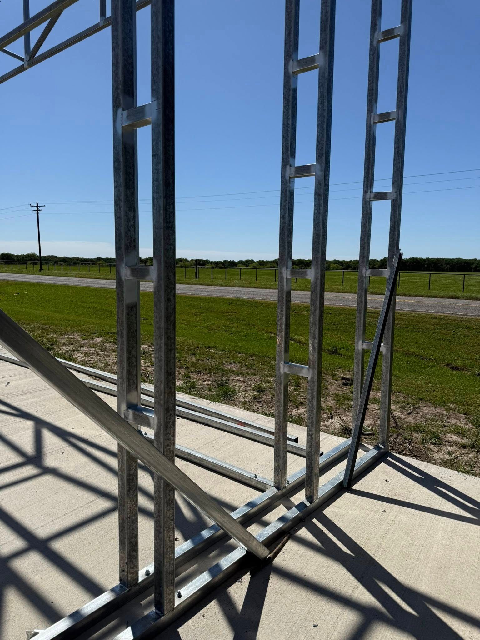 Metal frame construction on a concrete slab, outdoors on a sunny day.