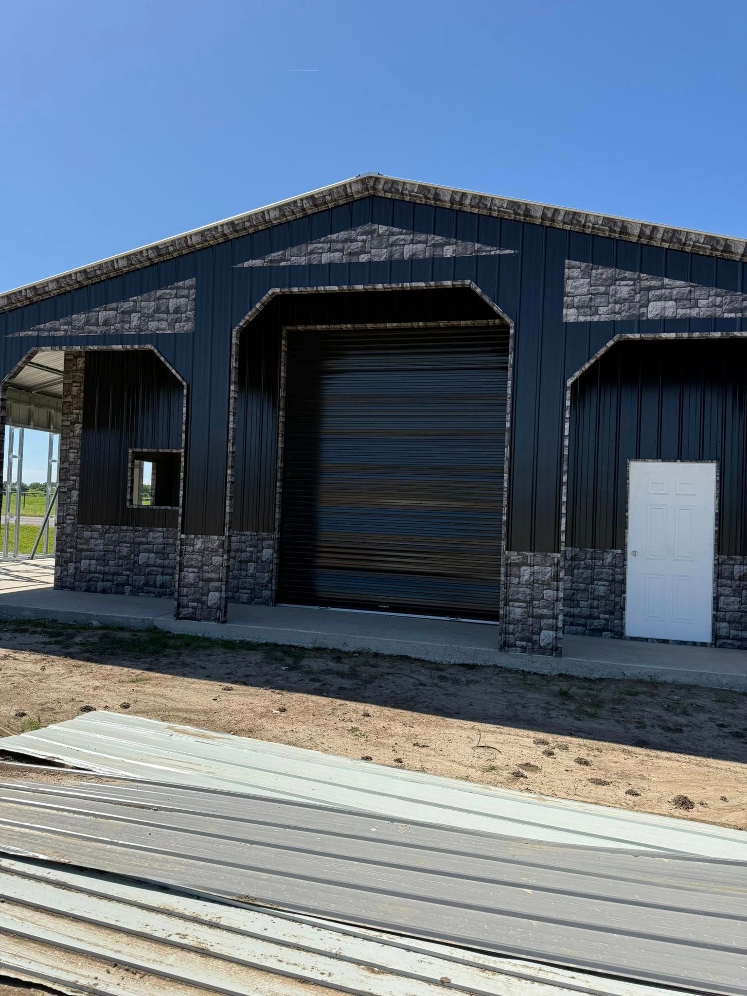 Black metal building with stone accents, large garage door, and white door, under a blue sky.