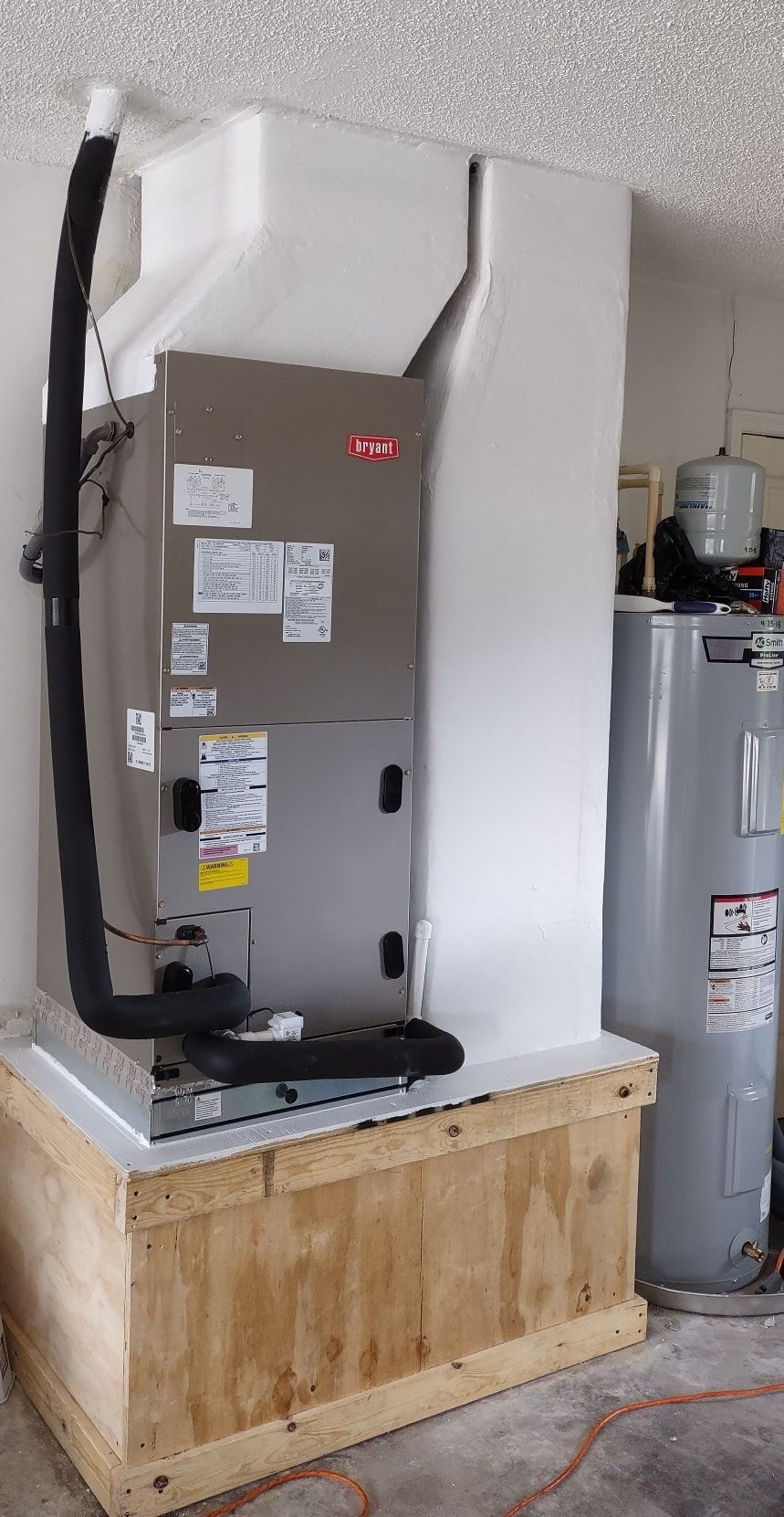 an air conditioner is sitting on top of a wooden box in a garage next to a water heater .