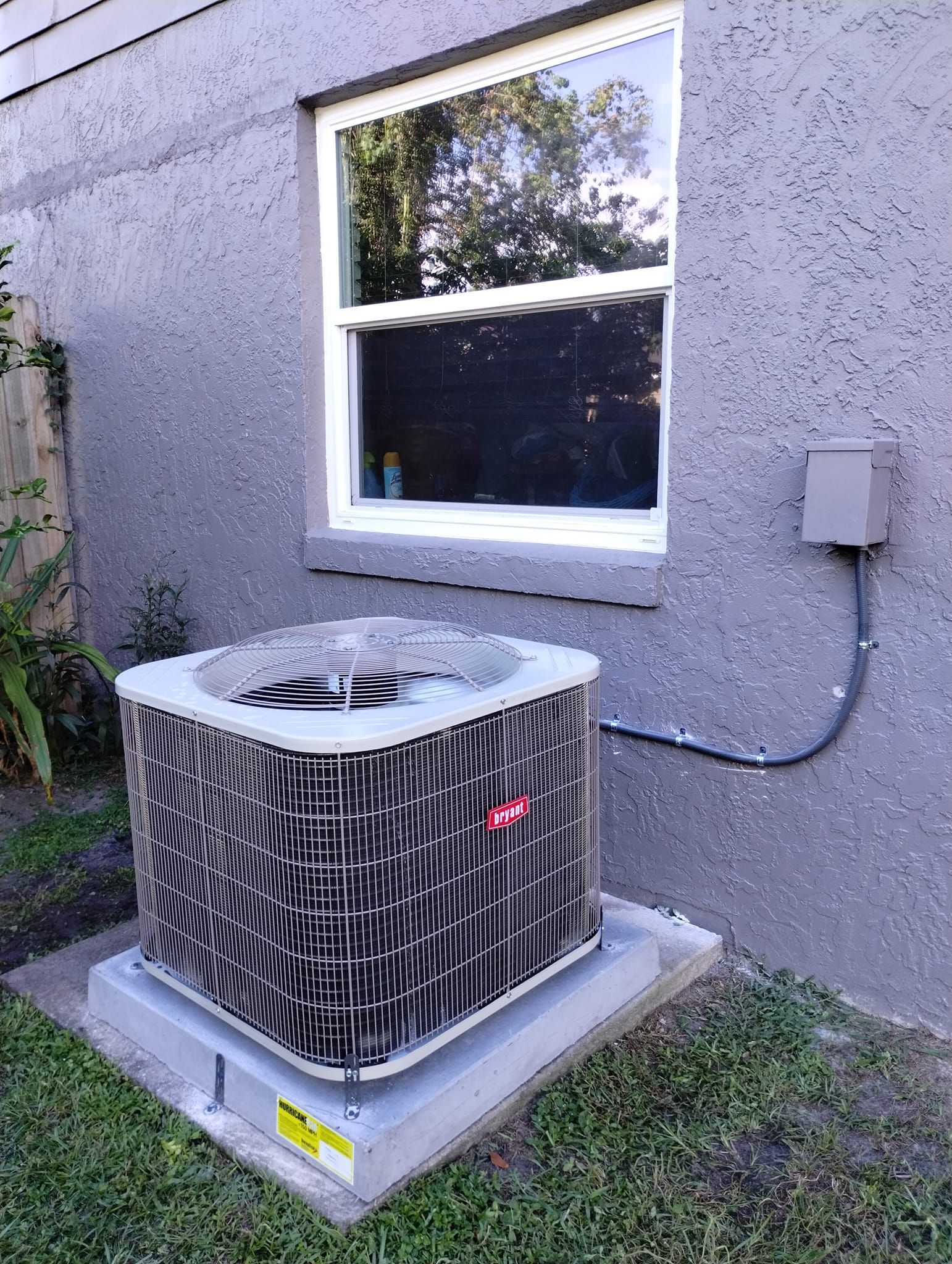 an air conditioner is sitting outside of a house next to a window .
