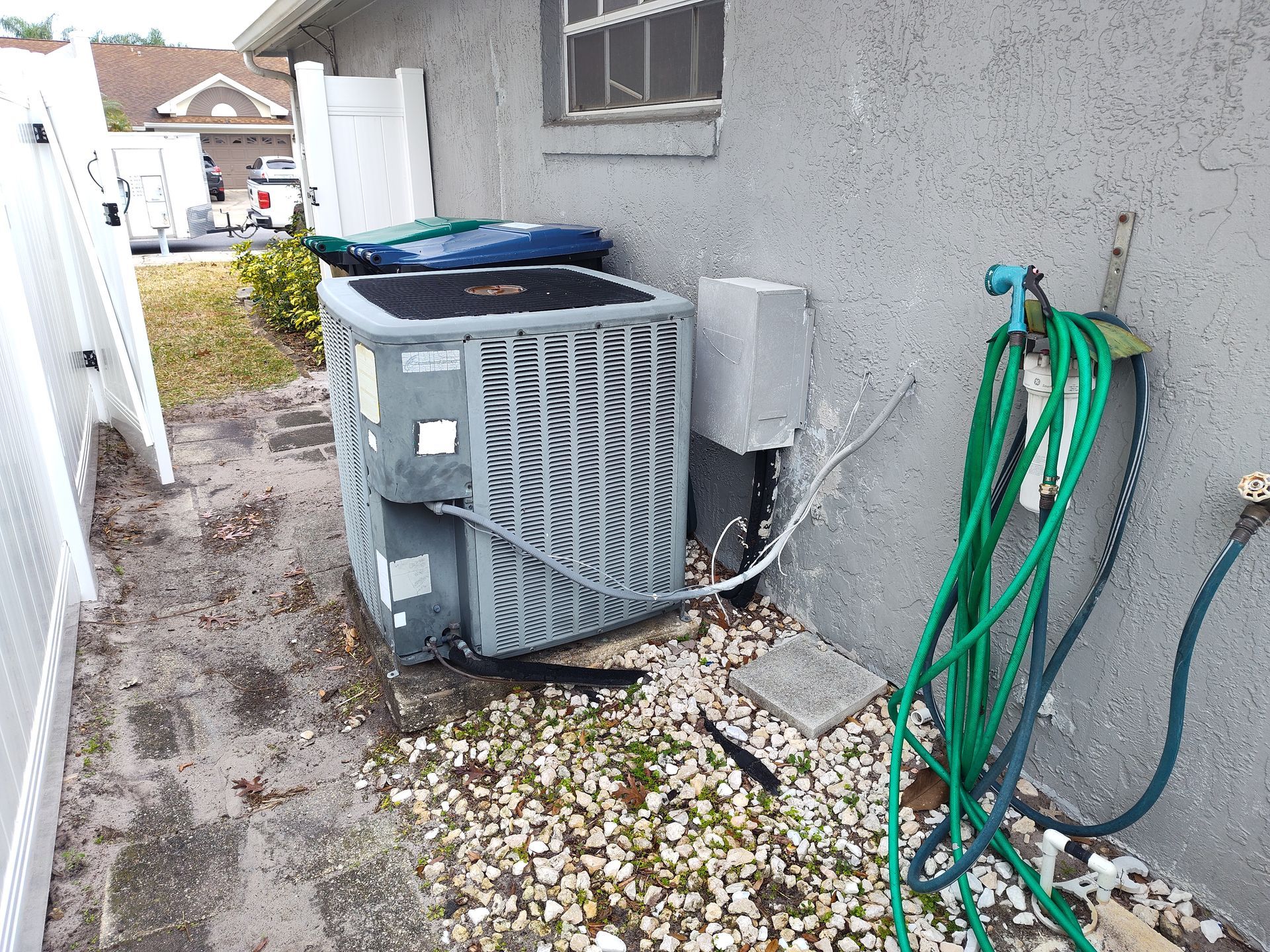 an air conditioner is sitting on the side of a house next to a hose .