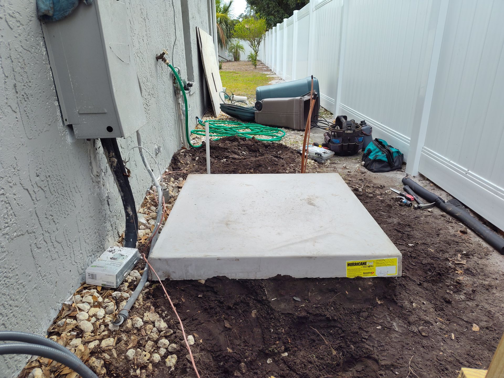 a concrete slab is sitting in the dirt in front of a white fence .