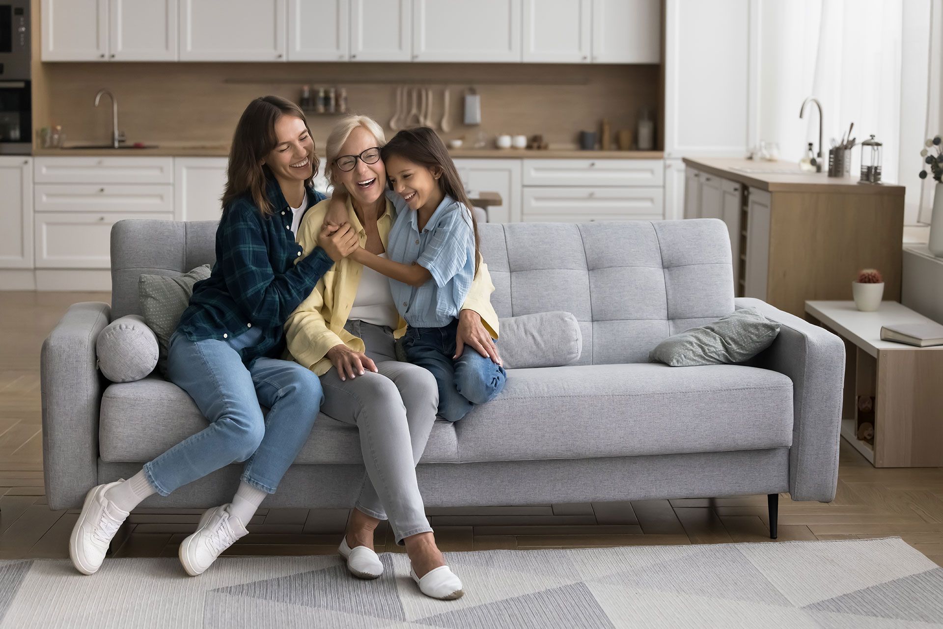 Woman, daughter, and granddaughter laughing together on a couch in a living room.