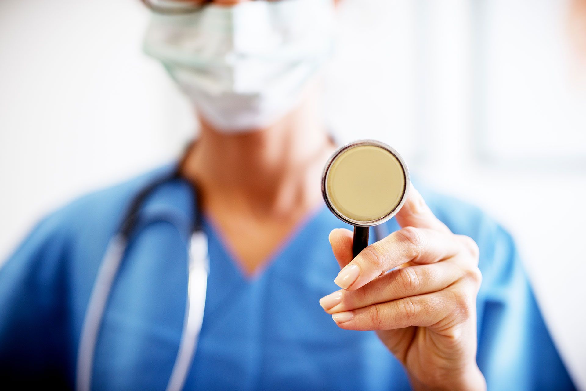 Nurse in blue scrubs holding stethoscope, ready for auscultation.