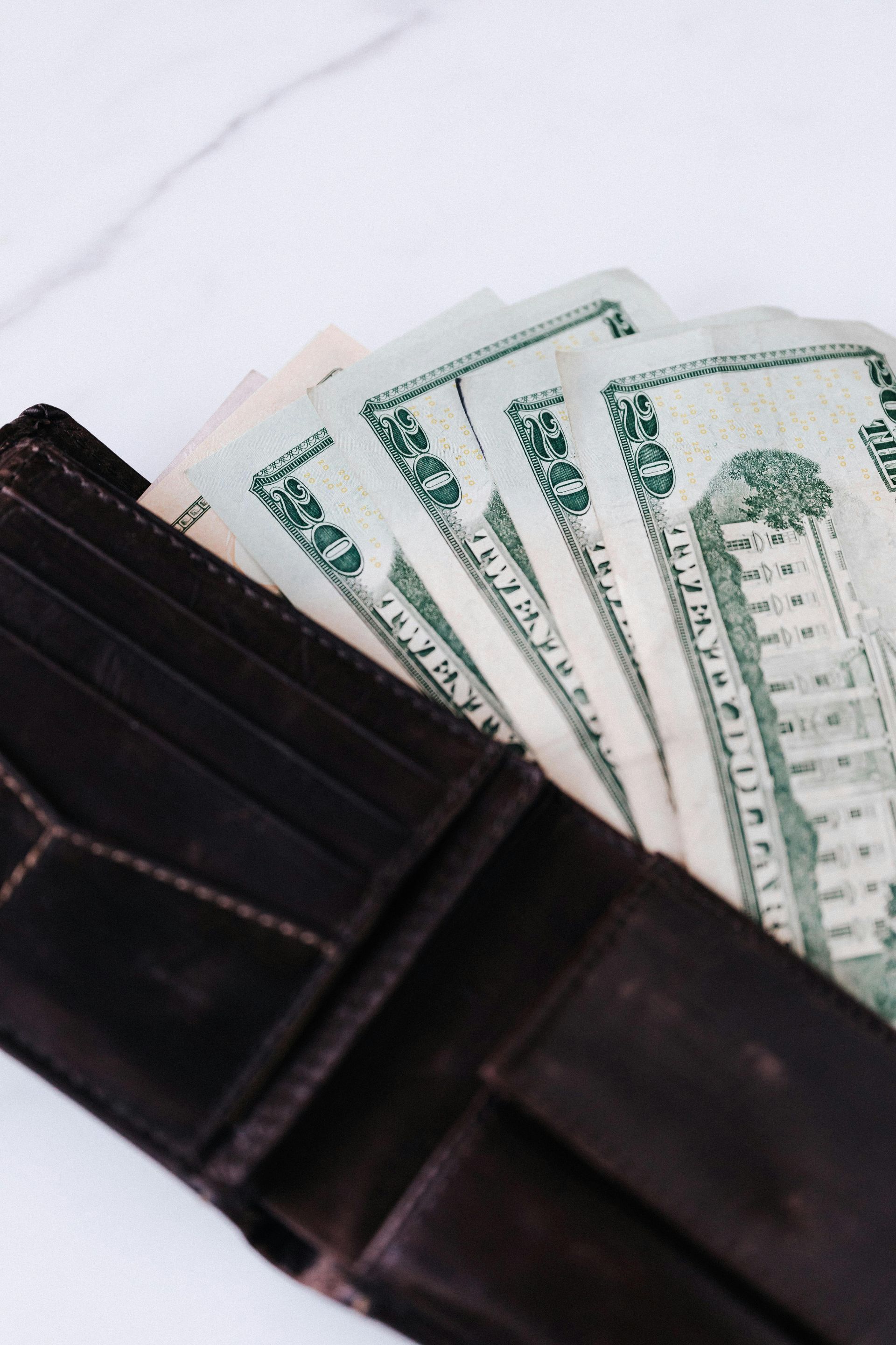 Open brown wallet with cash fanned out, on a white surface.