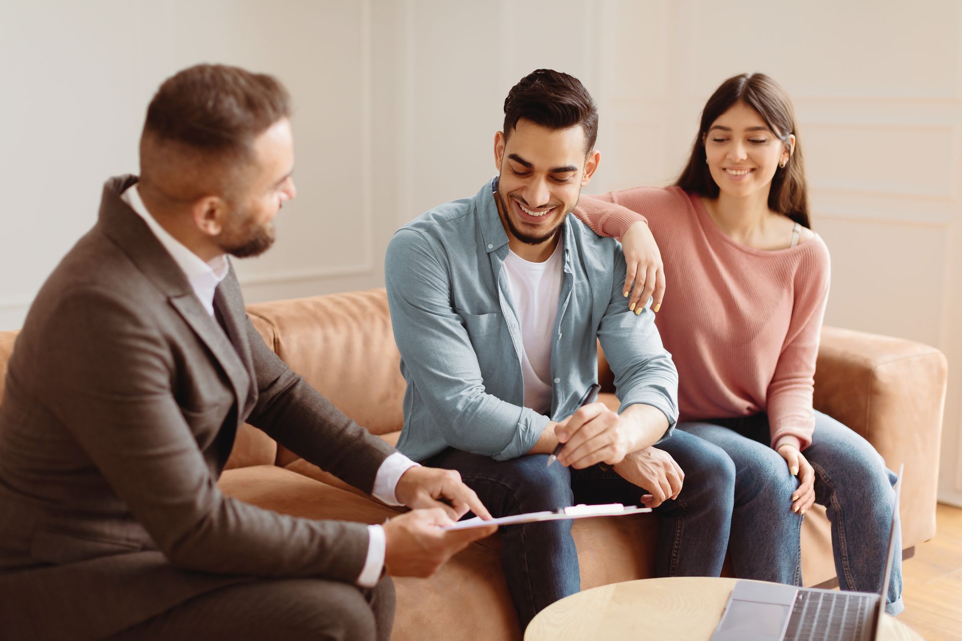 A financial advisor shows a phone to an older couple, reviewing documents at a table.