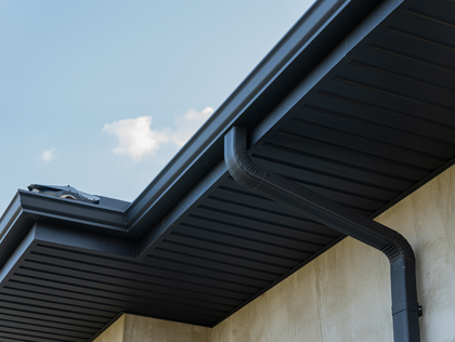 A dark gray roof overhang and gutter system attached to the side of a light-colored stucco building against a blue sky.