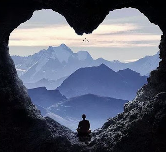 A Man Sits in a Cave Looking Out Over a Mountain Range