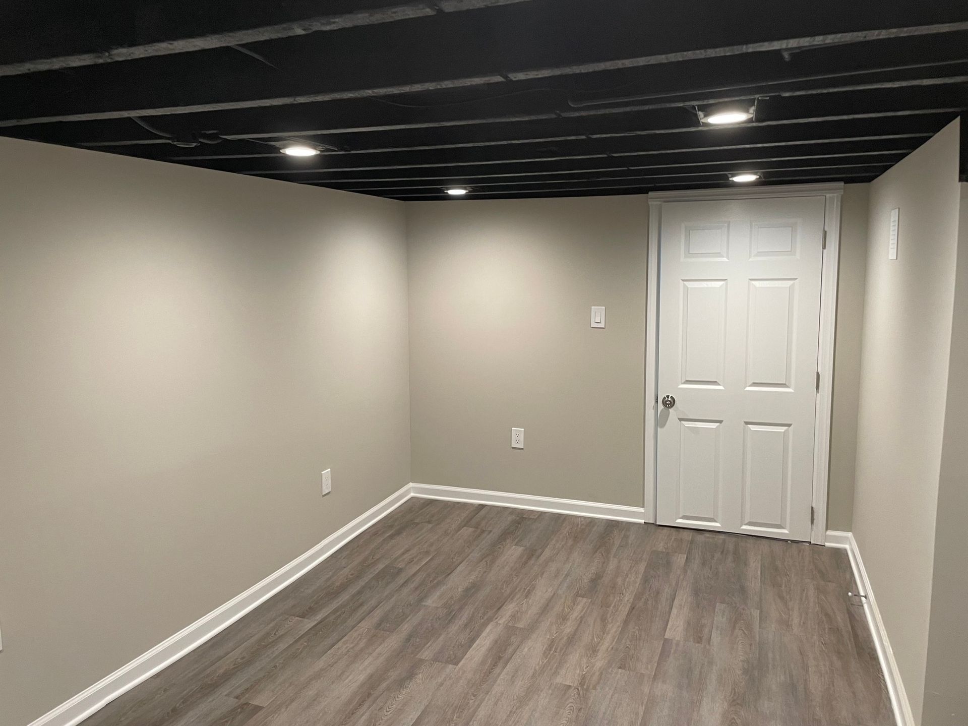 Empty room with gray walls, black ceiling, white door, and wood-look flooring.
