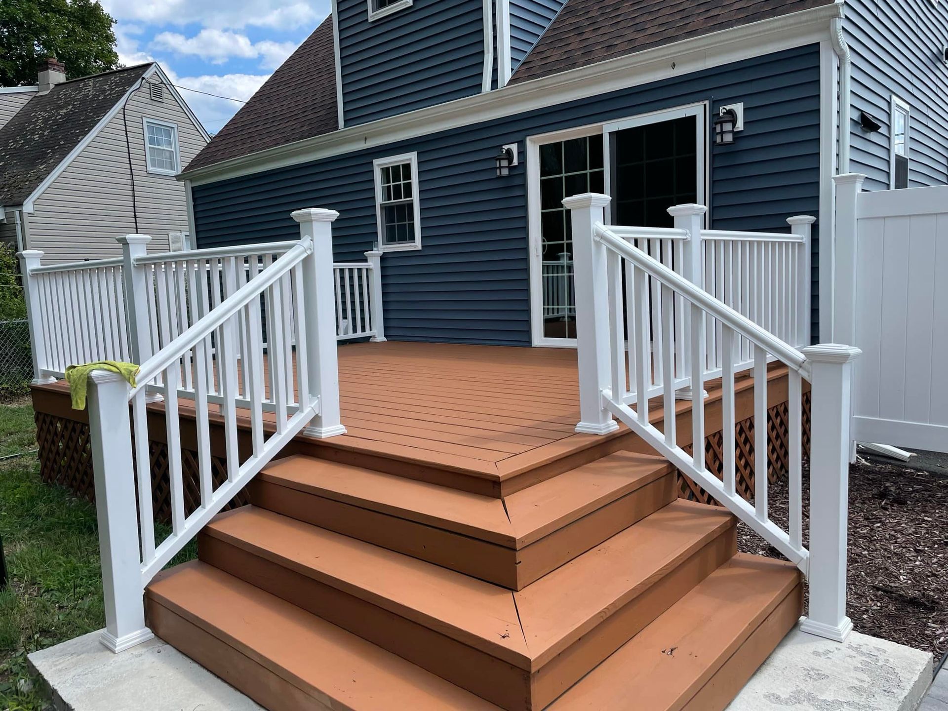 Brown deck with white railing and steps against a blue house with a sliding glass door.