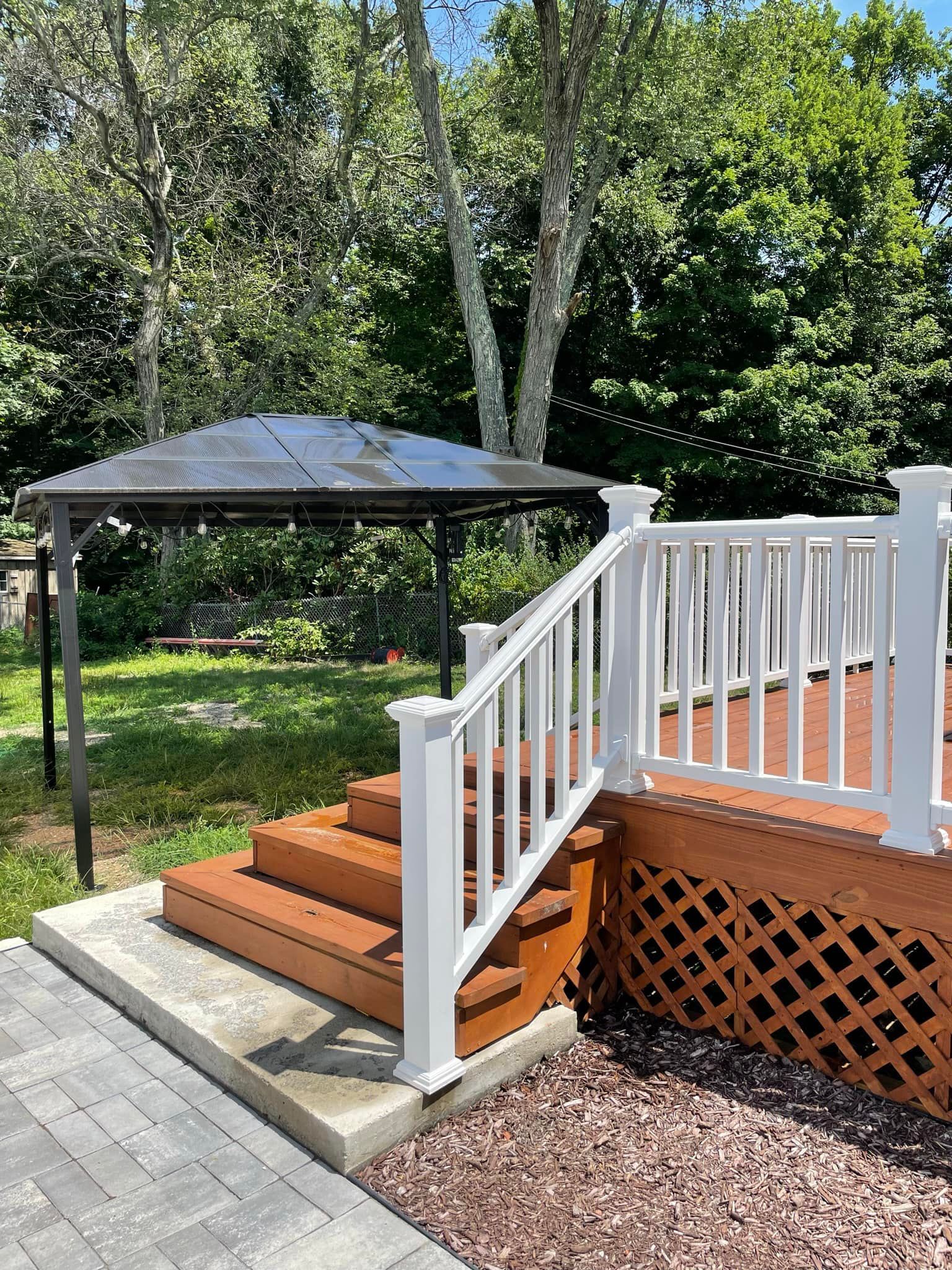 Wooden deck with stairs, white railing, and gazebo in a backyard setting.