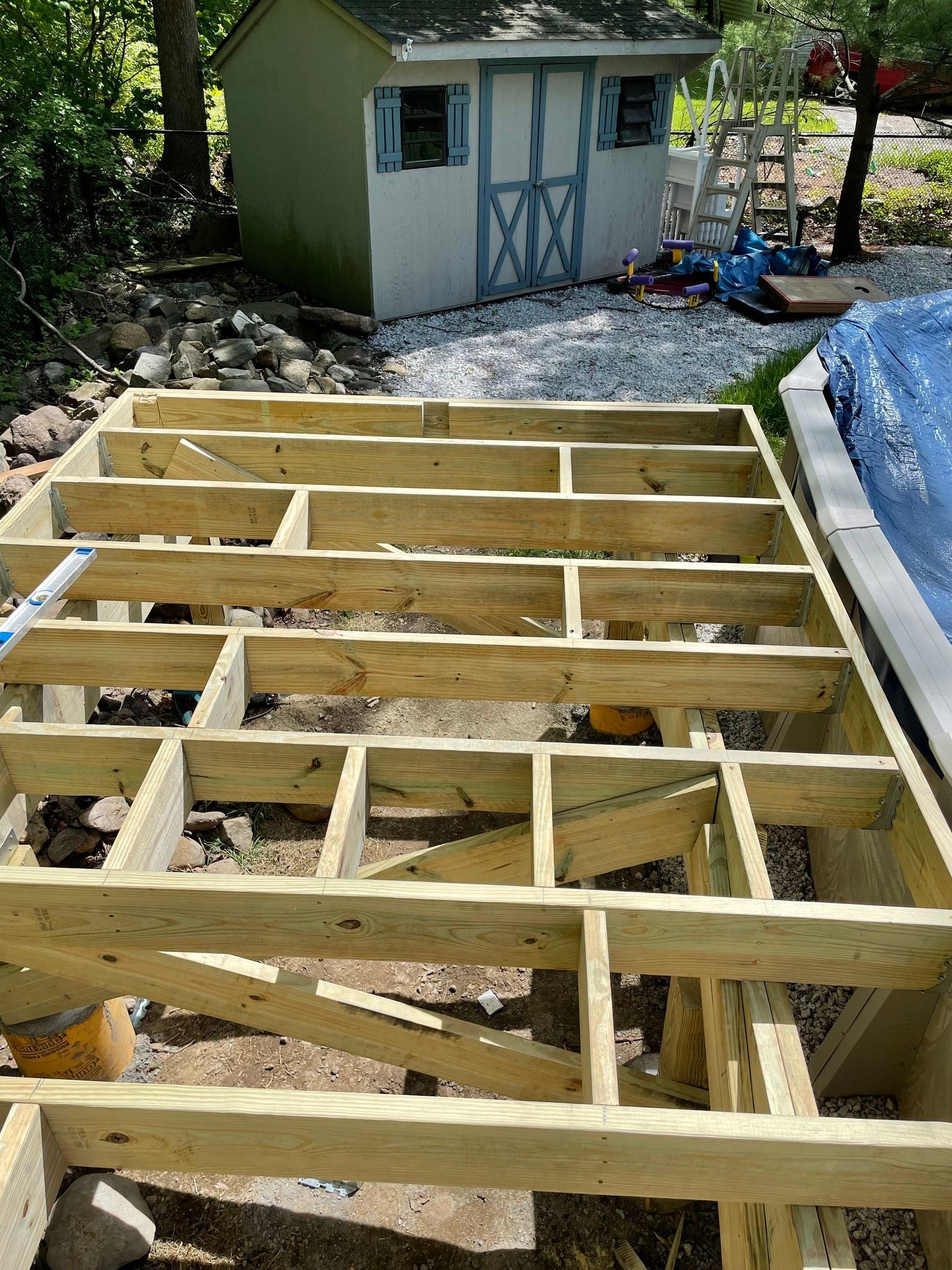 Wooden deck frame under construction outdoors with a shed in the background.