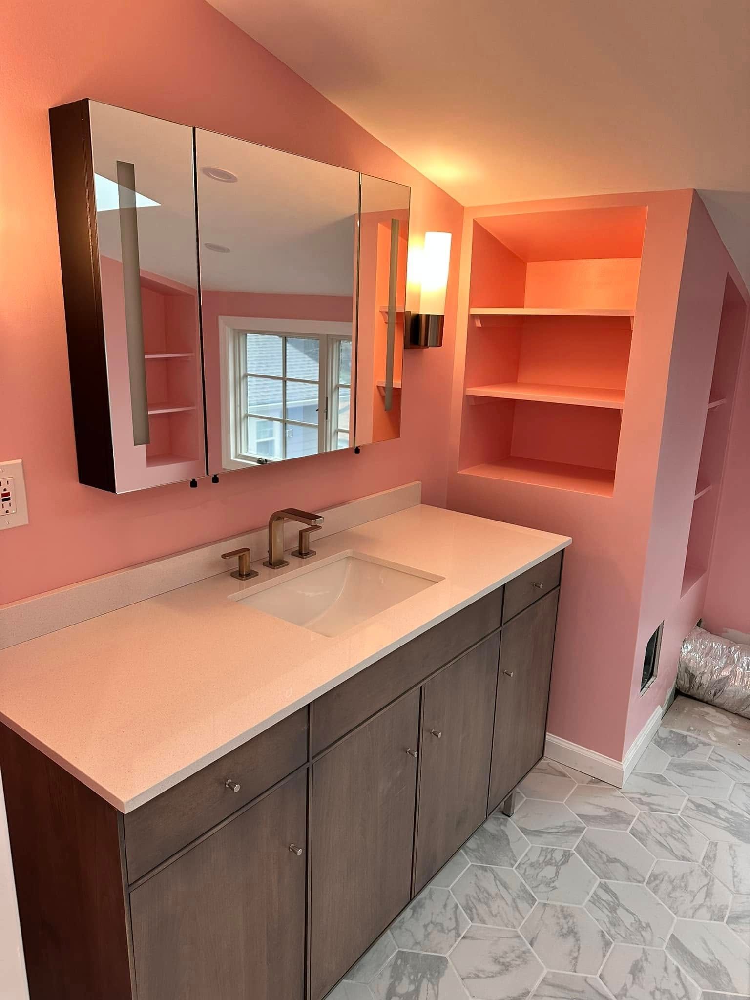 Pink bathroom with dark brown vanity, built-in shelves, and mirrored medicine cabinet.