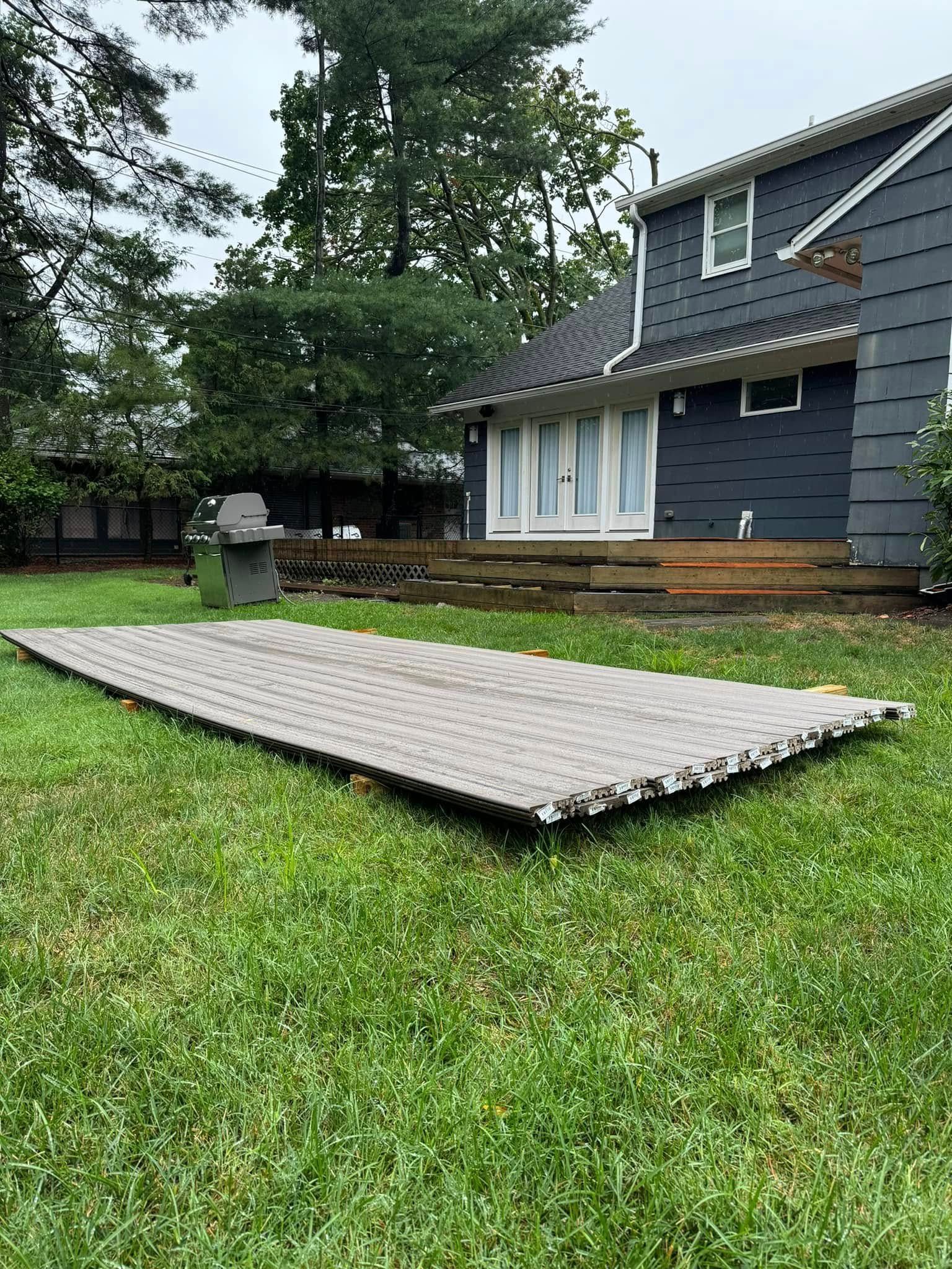 Gray mat on a grassy lawn near a wooden deck and a gray house.