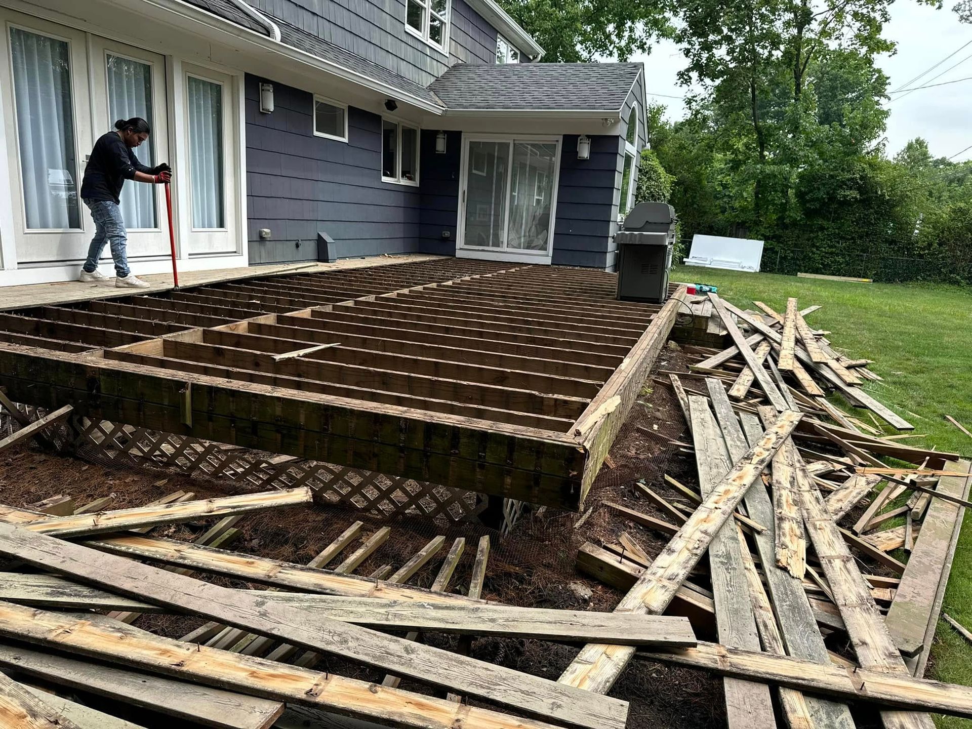 Deck demolition: A person works on removing old boards from a wooden deck in a backyard setting.
