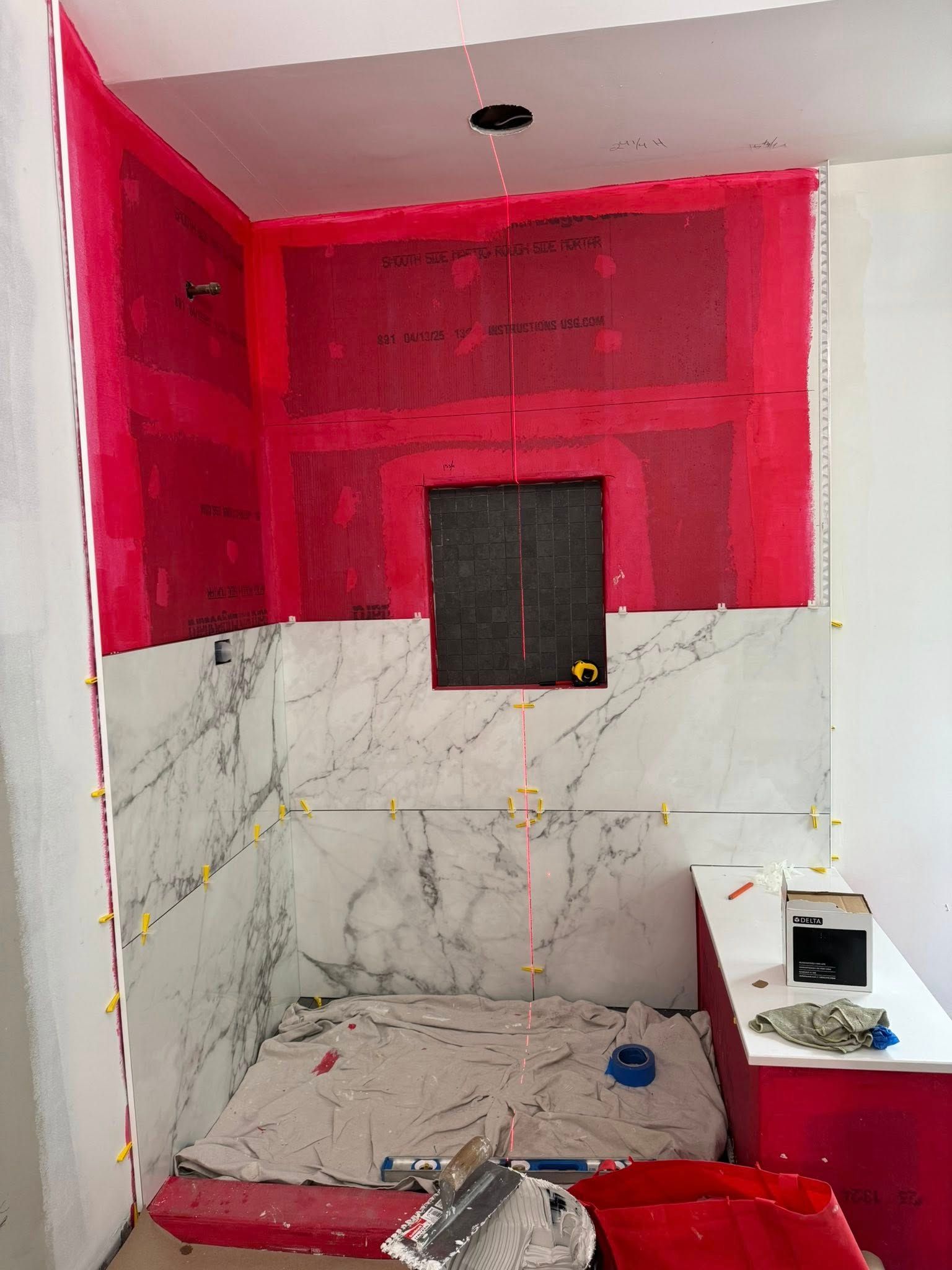 Bathroom under construction: red waterproofing membrane, marble tile, a niche, and a red tub.