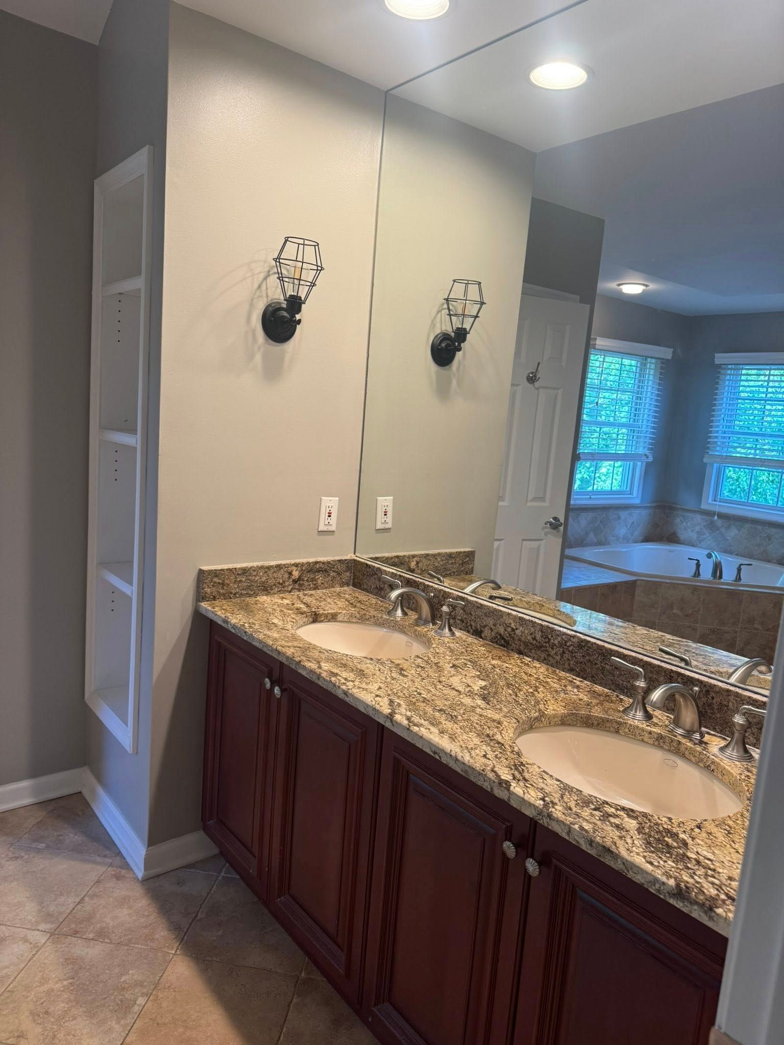 Bathroom with double sinks, granite countertop, red cabinets, large mirror, and recessed lighting.
