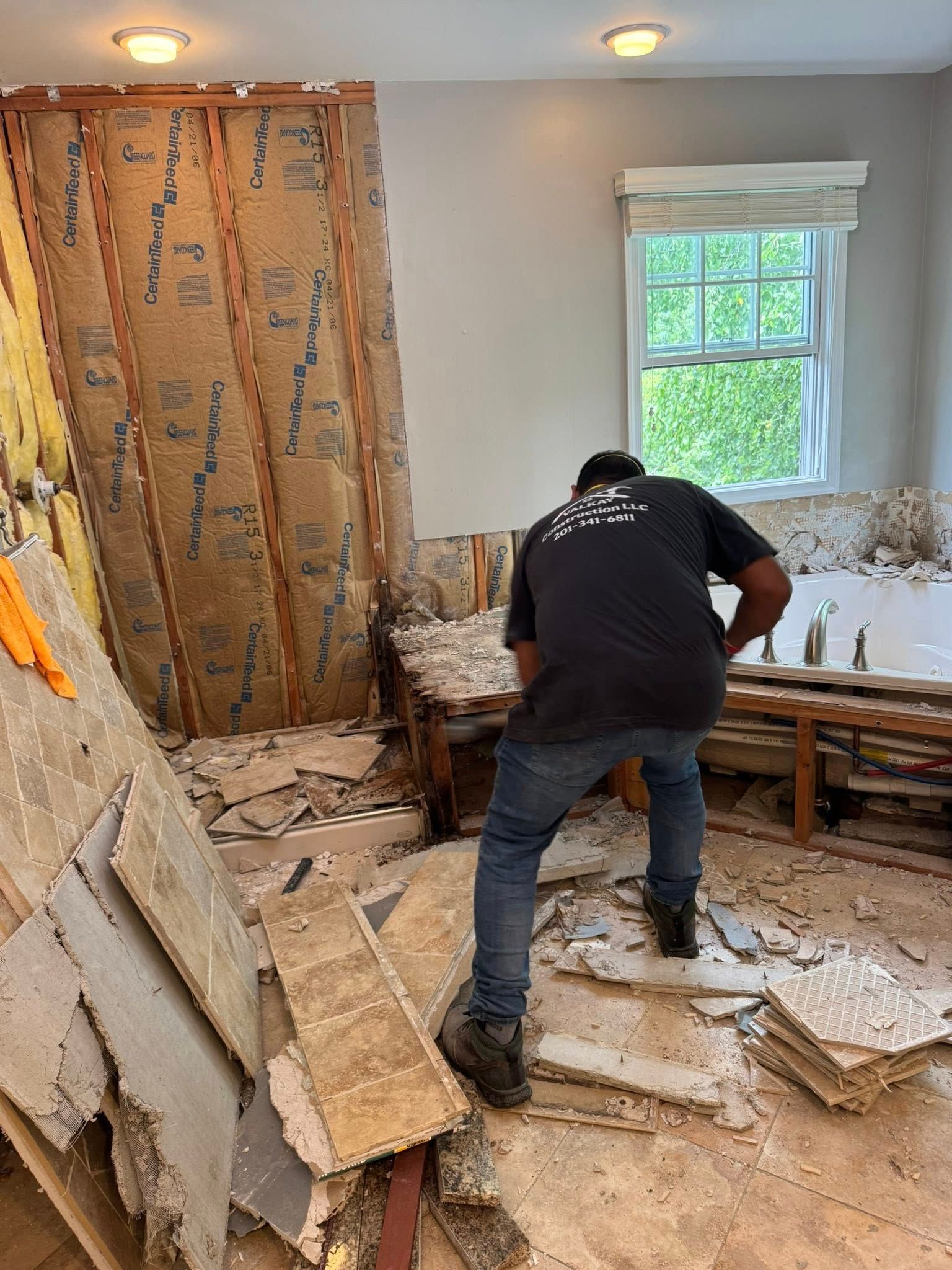Person demolishing a room; exposed wall studs, debris on floor, small window.