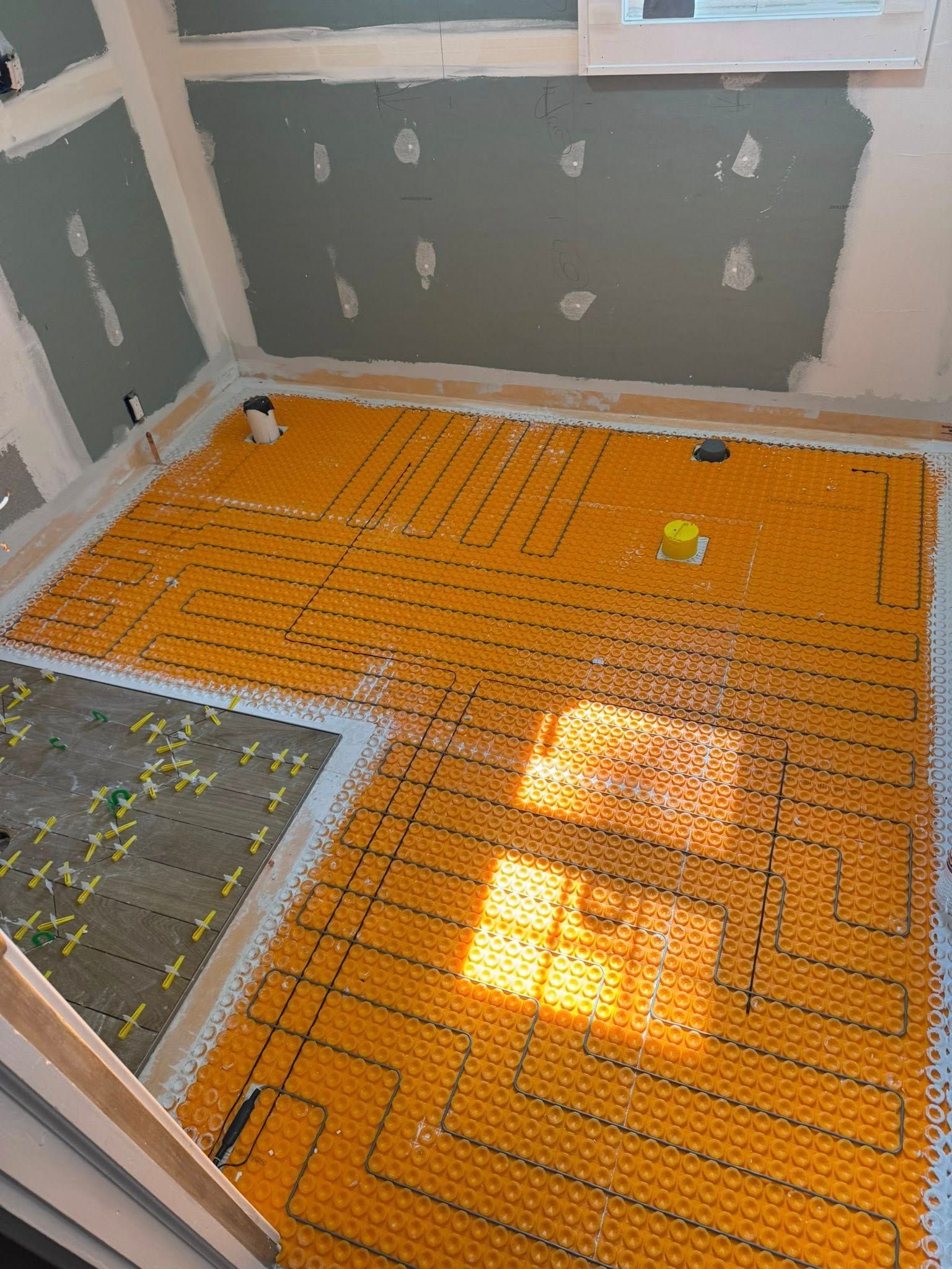 Construction of a room with installed radiant floor heating. Yellow tubing grid laid on subfloor. Unfinished walls.