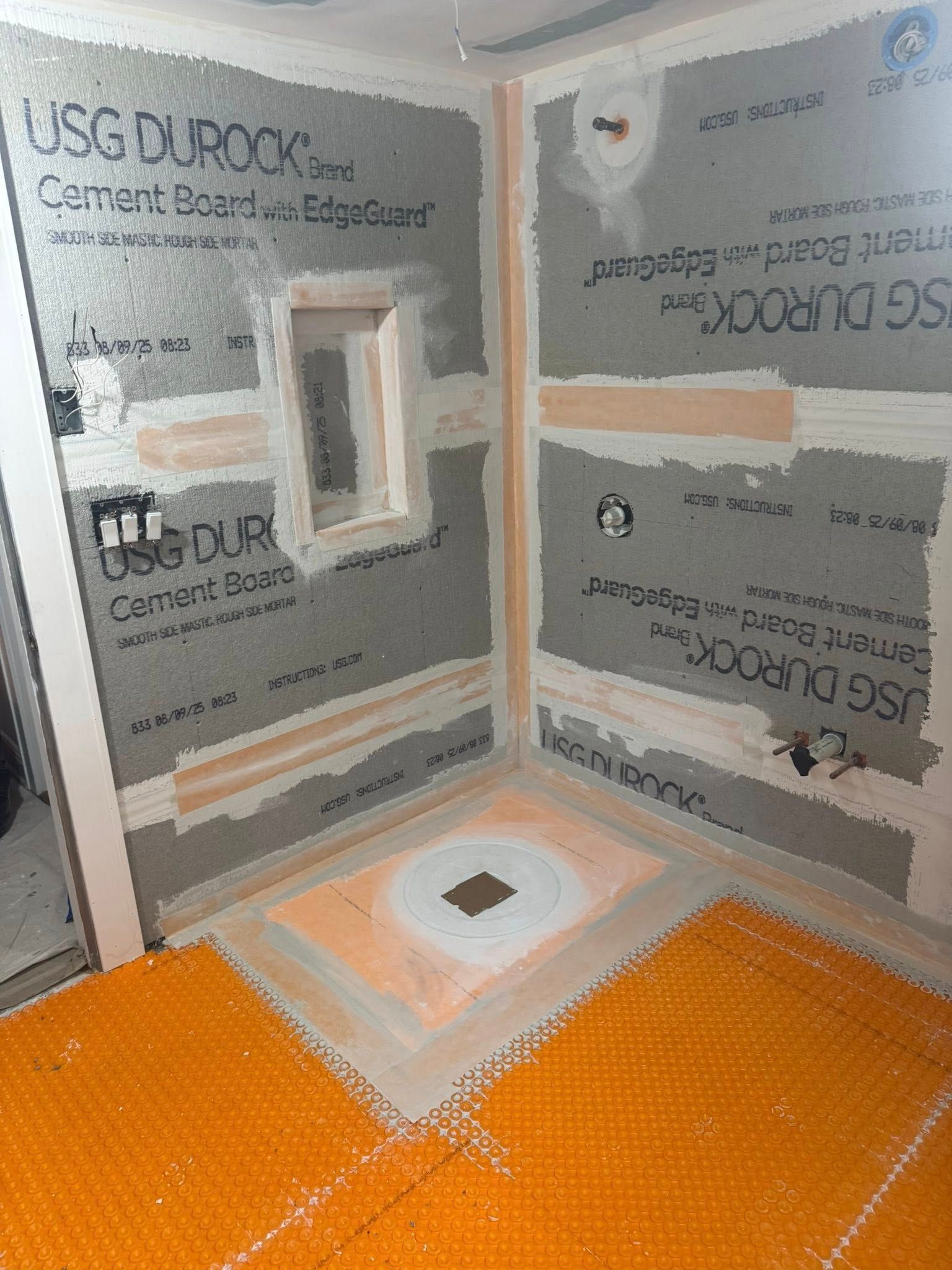 Shower under construction with gray cement board walls, orange membrane floor.