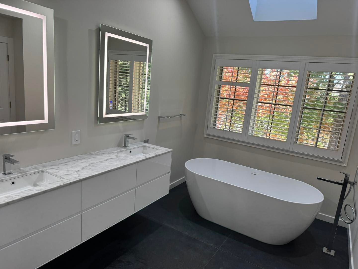 Modern bathroom with double vanity, free-standing tub, and large window with shutters; neutral colors.