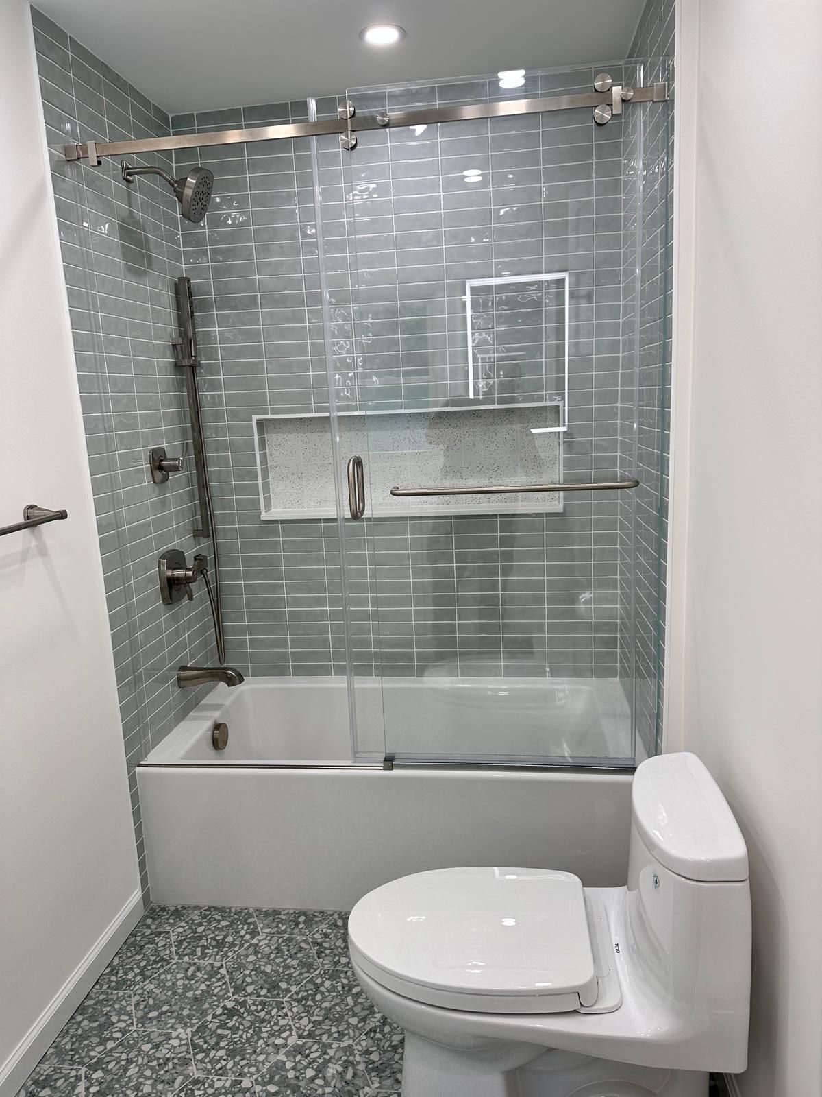 Bathroom with blue tiled shower, glass door, white tub, and toilet.