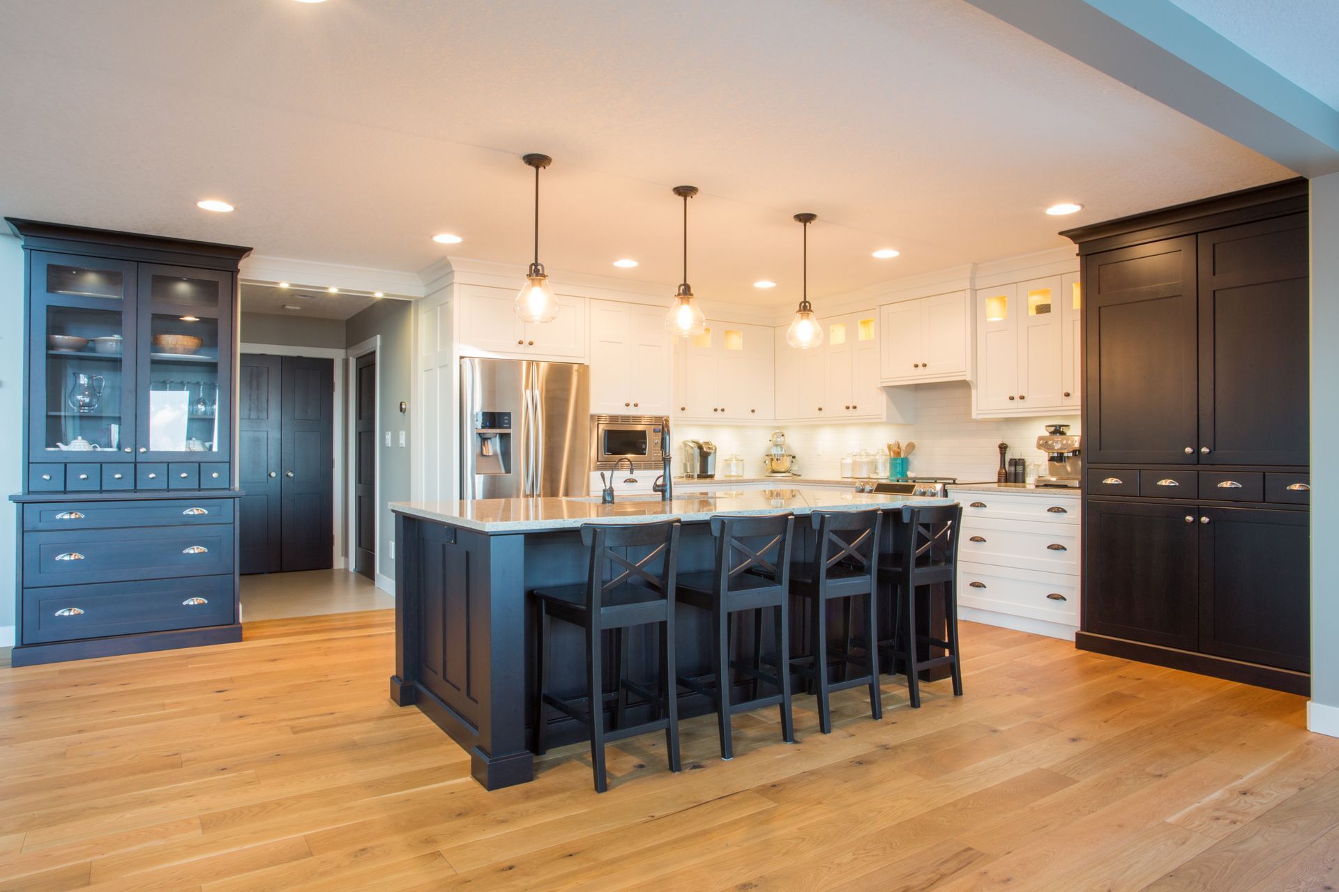 Modern kitchen with dark blue island, white cabinets, wood floors, and black chairs.
