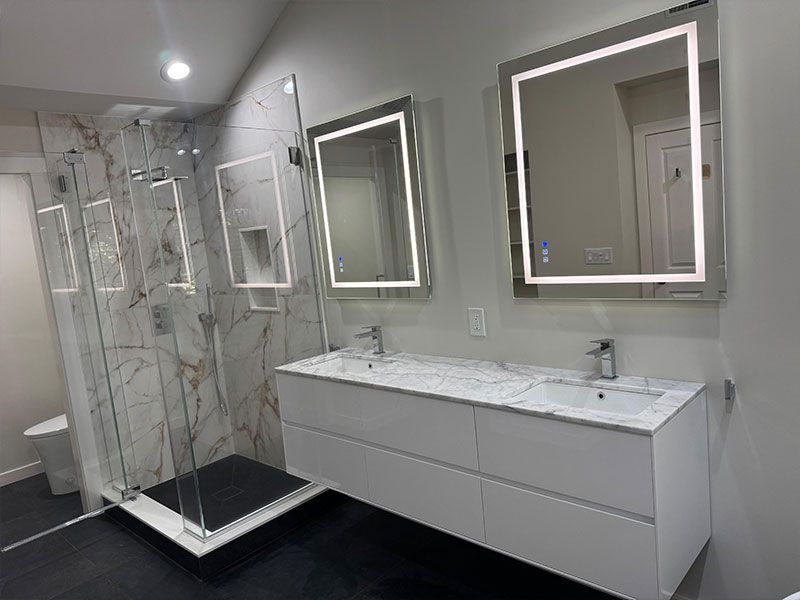 Modern bathroom with a marble shower, white vanity, and illuminated mirrors.
