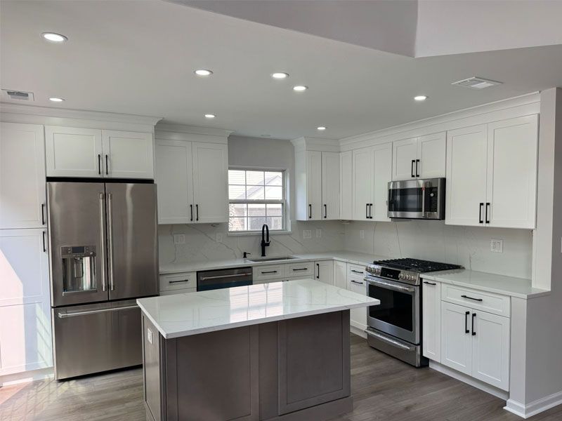 Modern white kitchen with stainless steel appliances, gray island, and white countertops.