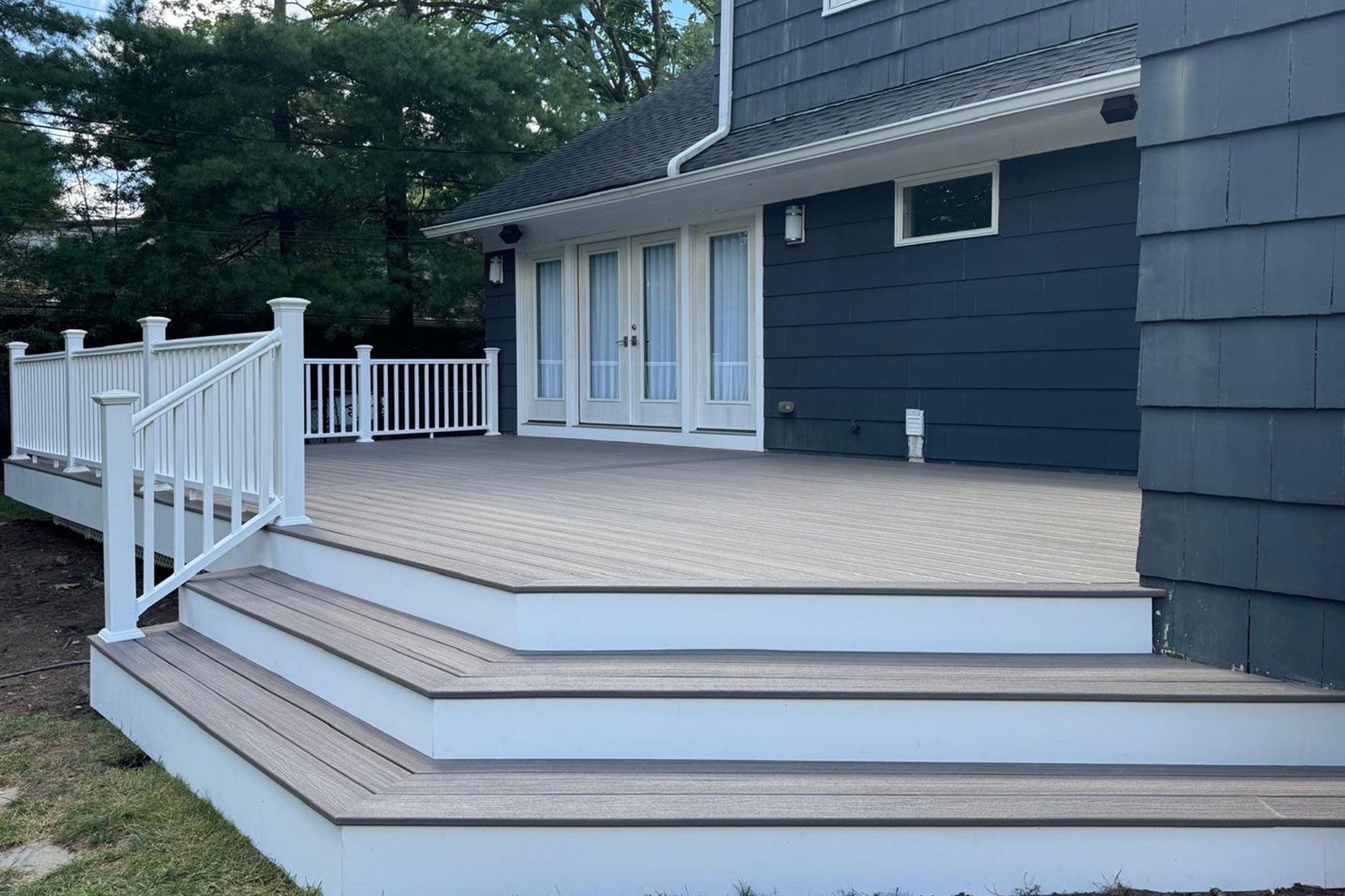 Wooden deck with white railing and stairs against a dark blue house.