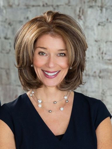 A woman wearing a black shirt and a pearl necklace is smiling.